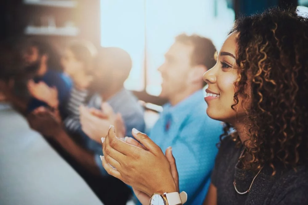 young woman smiling and clapping after hearing speaker in addiction recovery