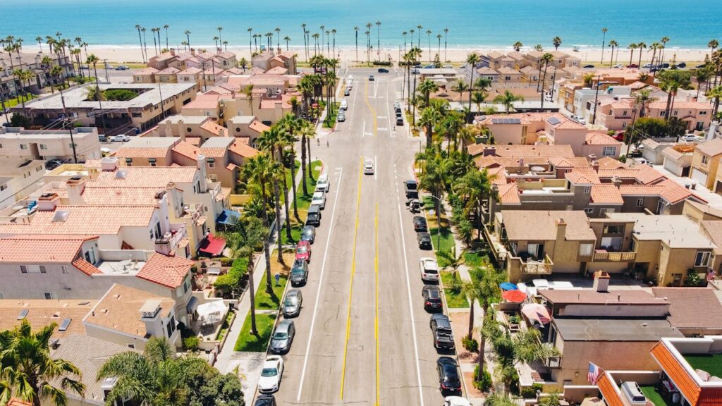 Aerial view of a sunny Southern California coastal neighborhood with palm-lined streets, residential homes, and the ocean visible in the background.